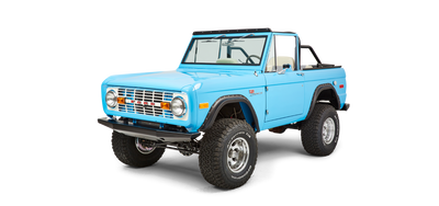 Front three-quarter view of bright blue Classic Ford Bronco with lifted stance and white interior.