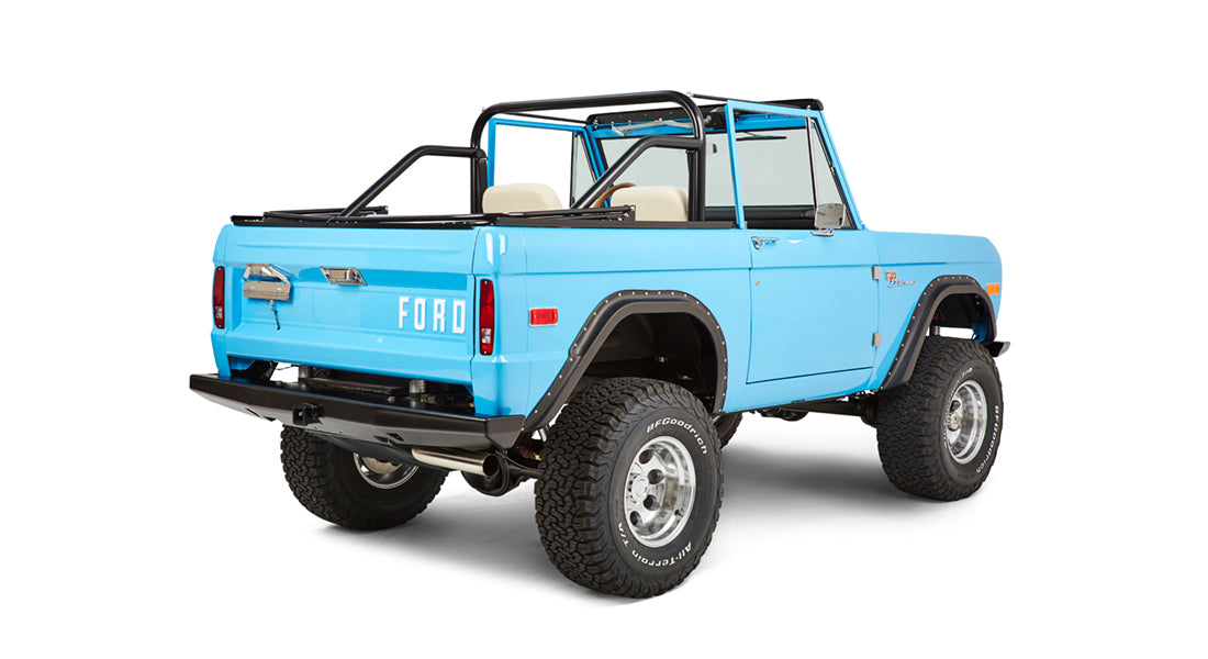 Three-quarter rear view of blue Classic Ford Bronco showing open top, rear gate, and off-road tires