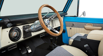 Interior of Classic Ford Bronco with wood steering wheel, plaid and leather seats, and manual shifters