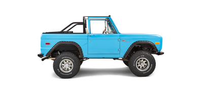Side view of a bright blue Classic Ford Bronco with off-road tires and no roof.