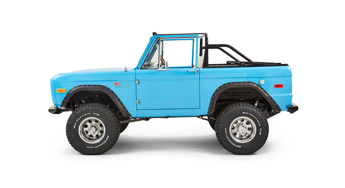 Classic Ford Bronco side view with driver door visible, blue body, and lifted suspension