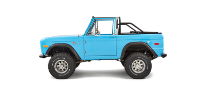 Side view of a bright blue Classic Ford Bronco with a black roll cage and no roof.