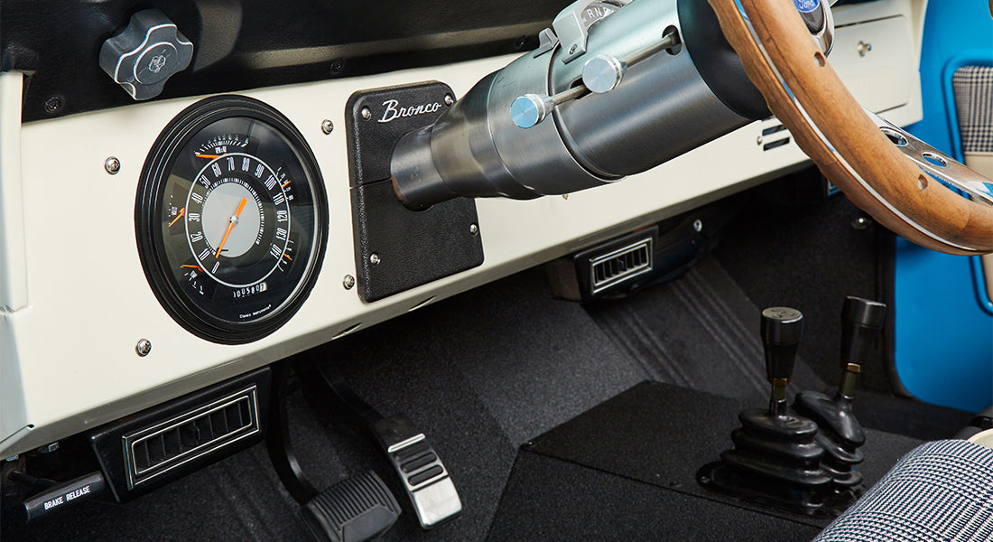 Dashboard of Classic Ford Bronco featuring round speedometer, wood steering wheel, and manual controls