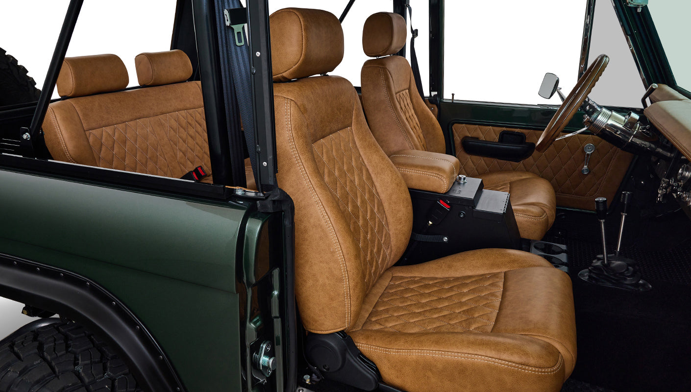 Side view of tan diamond-stitched front seats inside Classic Ford Bronco with door open.