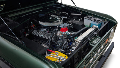 Classic Ford Bronco engine bay with detailed engine components and bright battery.