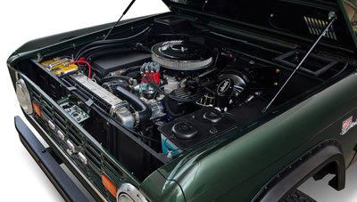Classic Ford Bronco angled view of engine bay with open hood, showing detailed engine components and dark green fender