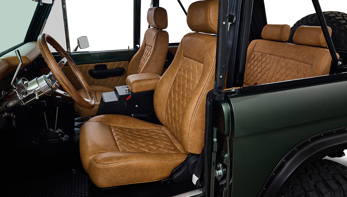 Interior view of Classic Ford Bronco showing tan diamond-stitched front seats and steering wheel.