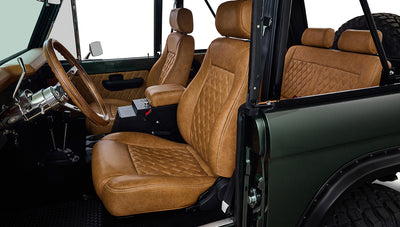 Interior view of Classic Ford Bronco showing tan diamond-stitched front seats and steering wheel.