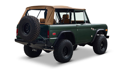 Three-quarter rear view of Classic Ford Bronco in dark forest green with tan soft top and spare tire on white background