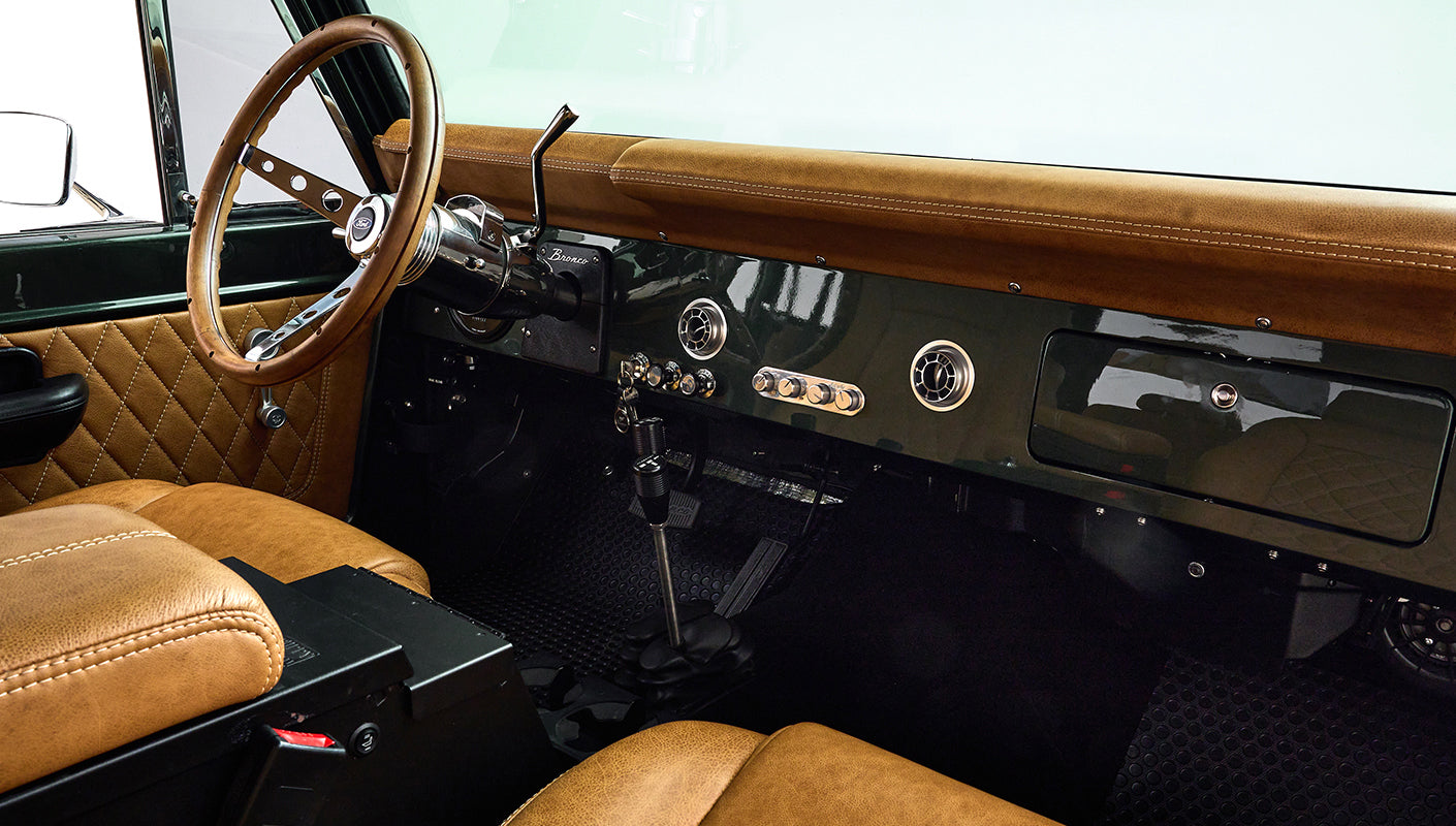 Steering wheel and dashboard of Classic Ford Bronco featuring tan upholstery and vintage controls
