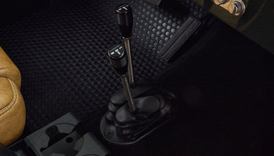 Two gear levers with black round knobs next to tan leather seat in Classic Ford Bronco interior