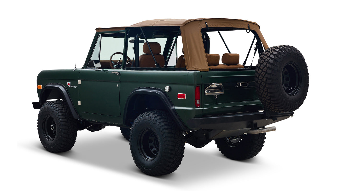 Three-quarter rear view of Classic Ford Bronco in dark forest green with tan soft top and spare tire on white background
