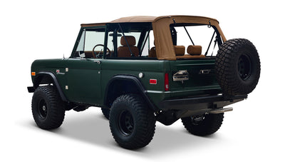 Three-quarter rear view of Classic Ford Bronco in dark forest green with tan soft top and spare tire on white background
