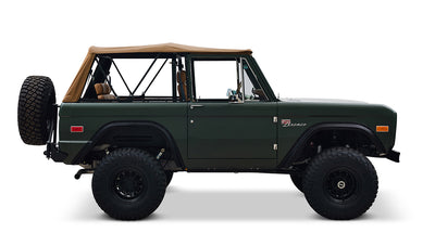 Side view of Classic Ford Bronco in dark forest green with tan soft top and large off-road tires