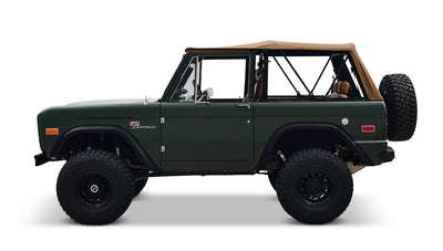 Side view of Classic Ford Bronco in dark forest green with tan soft top and large off-road tires