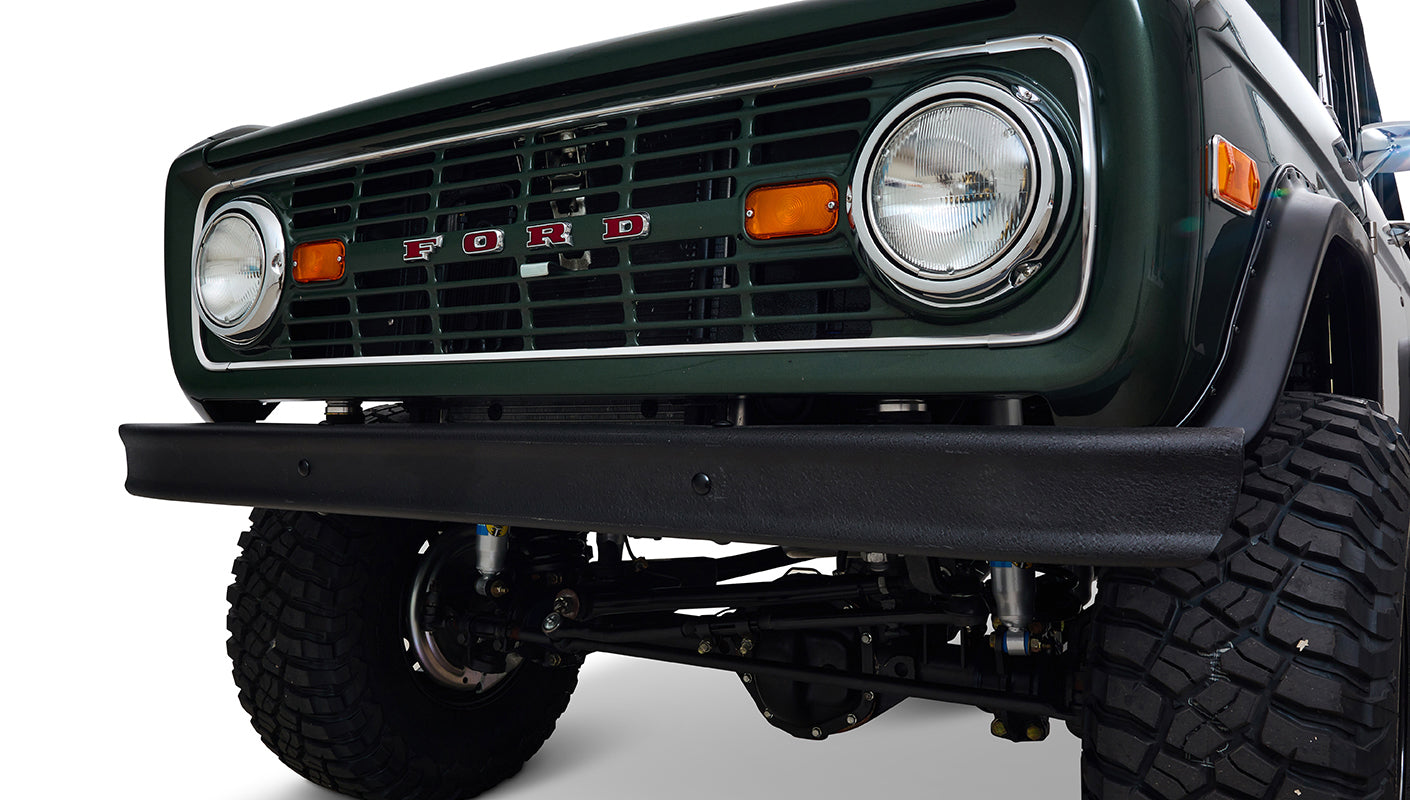 Front grill and bumper of Classic Ford Bronco in dark forest green with visible headlights and orange lights.