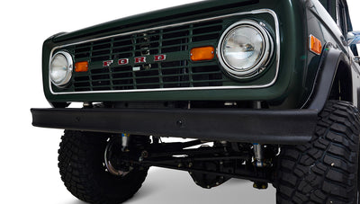 Front grill and bumper of Classic Ford Bronco in dark forest green with visible headlights and orange lights.