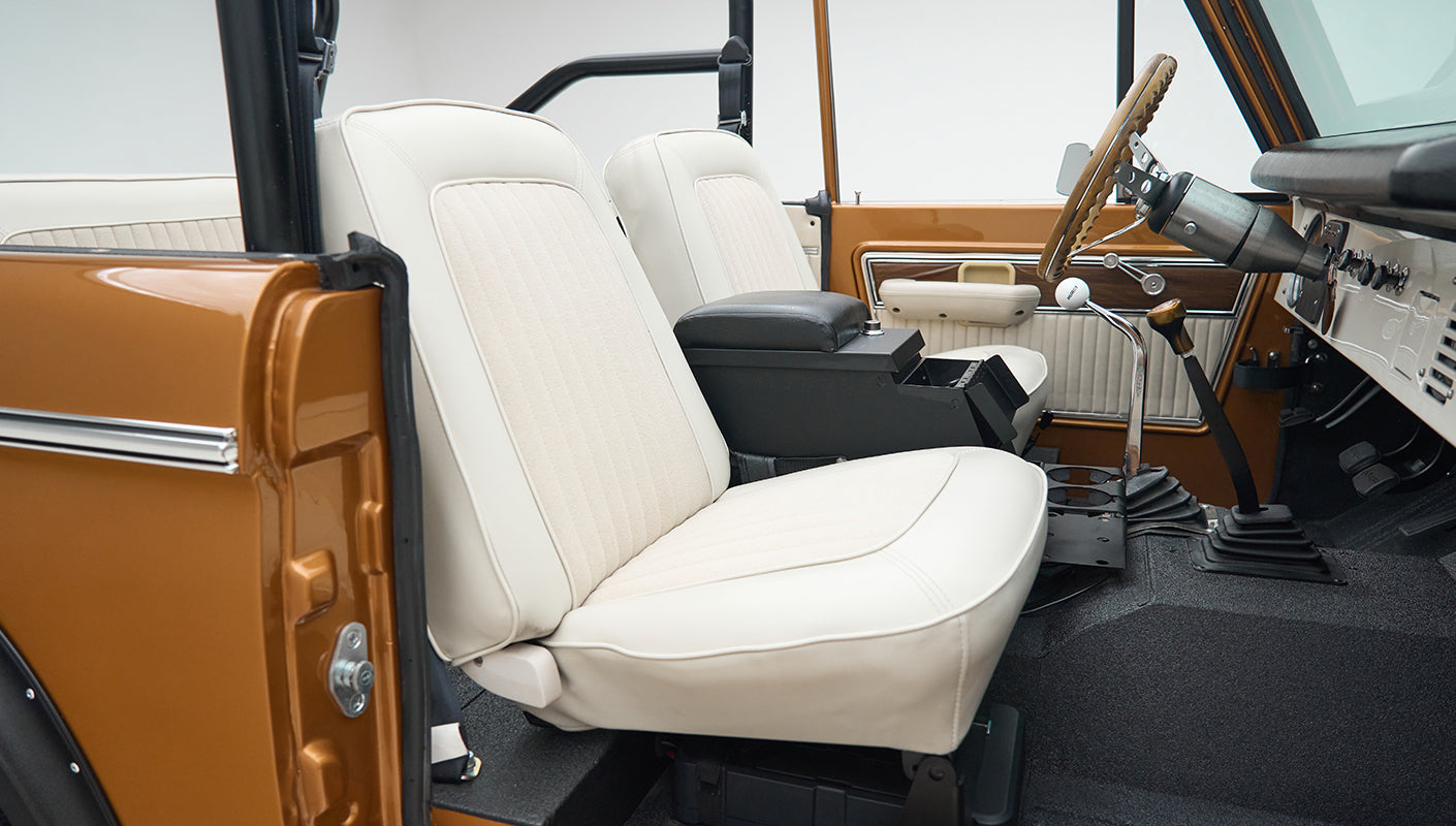 Driver side interior view of Classic Ford Bronco showing white seats, black floor, and dashboard