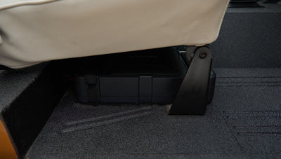 Black electronic device mounted under a white seat inside Classic Ford Bronco