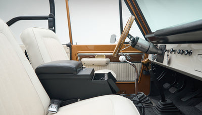 Driver side interior of Classic Ford Bronco with wood panel door, white seats, and black center console