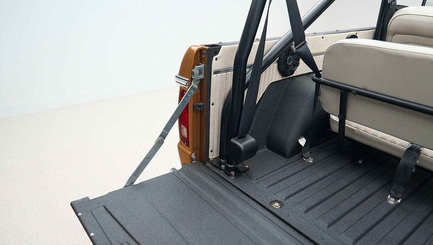 Open rear cargo area of Classic Ford Bronco showing black bed liner and rear seat