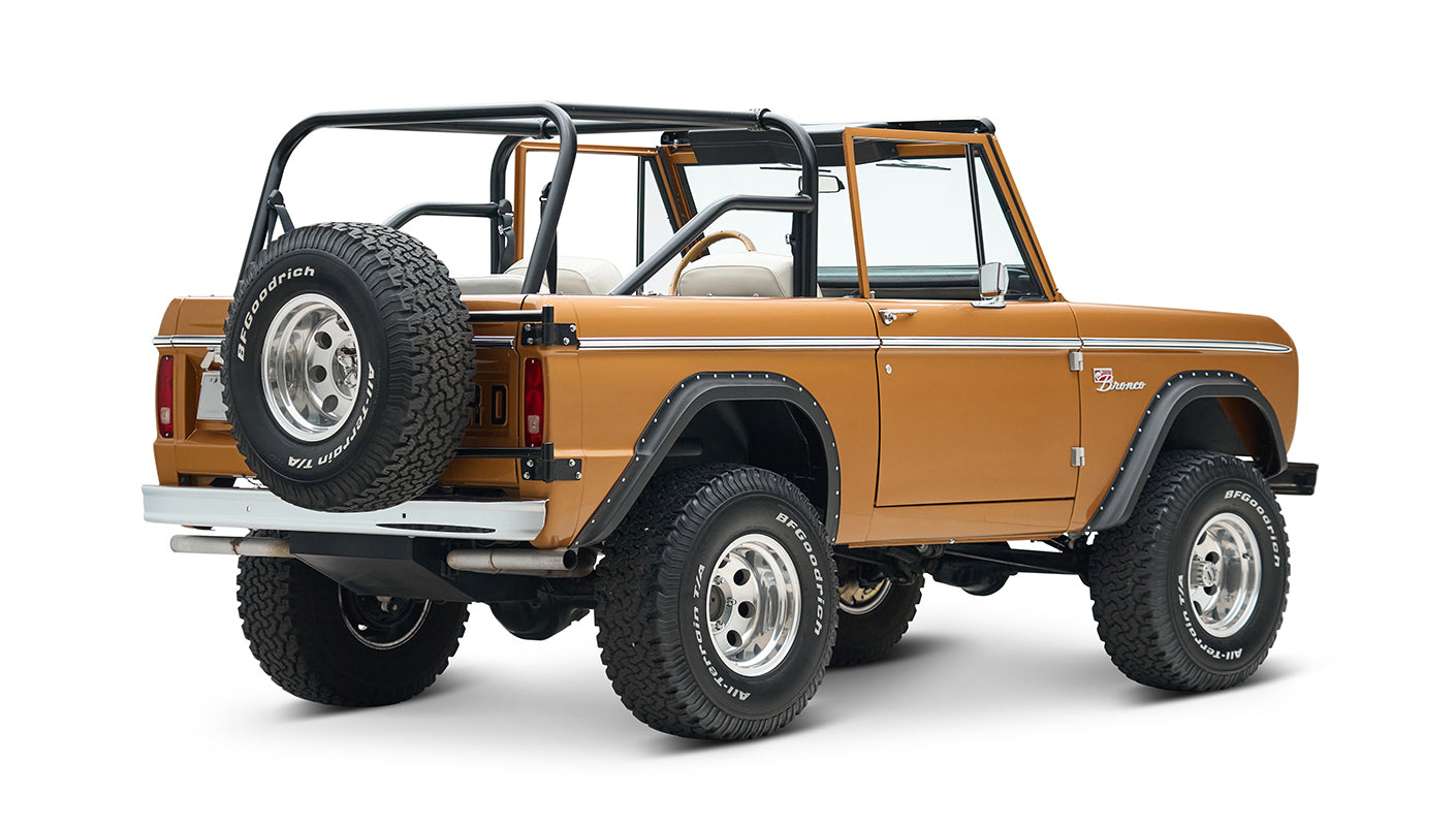 Rear-side view of open-top Classic Ford Bronco in saddle bronze with black roll cage and white seats on white background