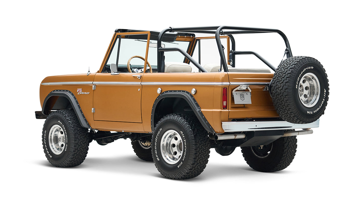 Rear-side view of saddle bronze Classic Ford Bronco with spare tire mounted on tailgate on white background