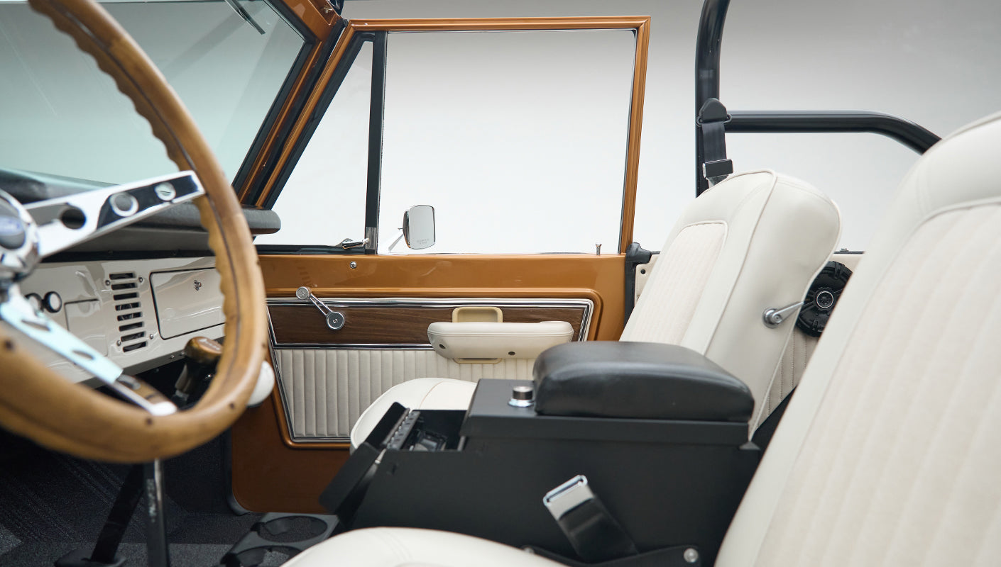 Classic Ford Bronco interior side view with white seats, wood panel door, and steering wheel