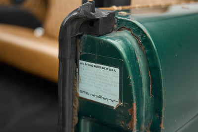Rusty white vehicle identification label on green painted metal door frame