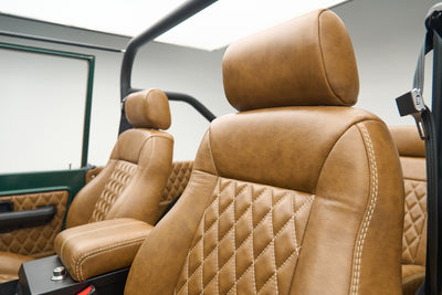 Close-up of tan leather quilted front seats inside vehicle with roll cage