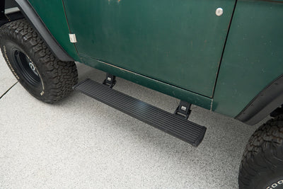 Black running board mounted below green vehicle door with large tire nearby