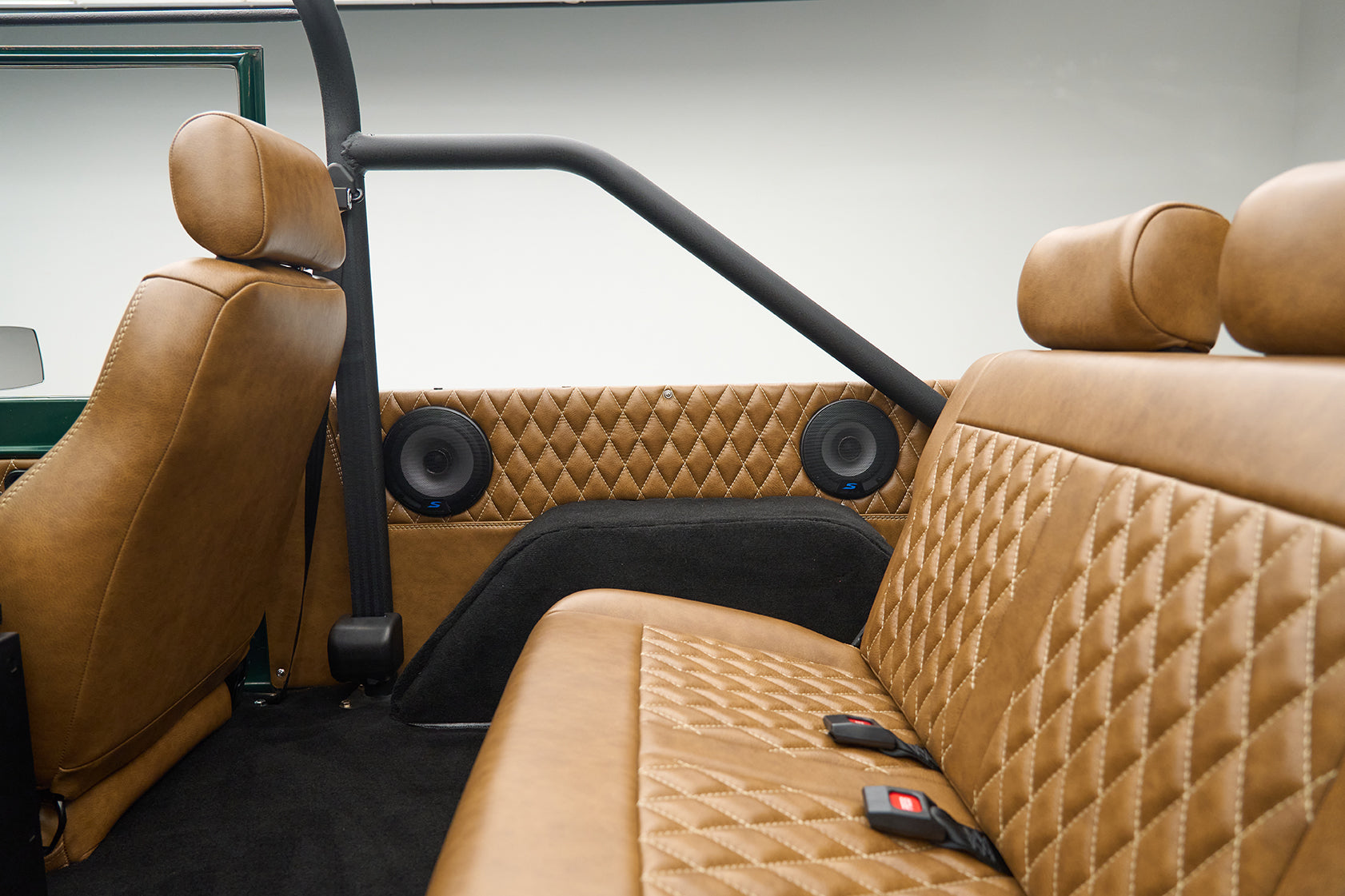 Rear side view of tan leather quilted bench seat and black roll cage inside vehicle