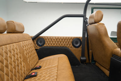 Wide rear interior view of tan leather seats, black roll cage, and two speakers
