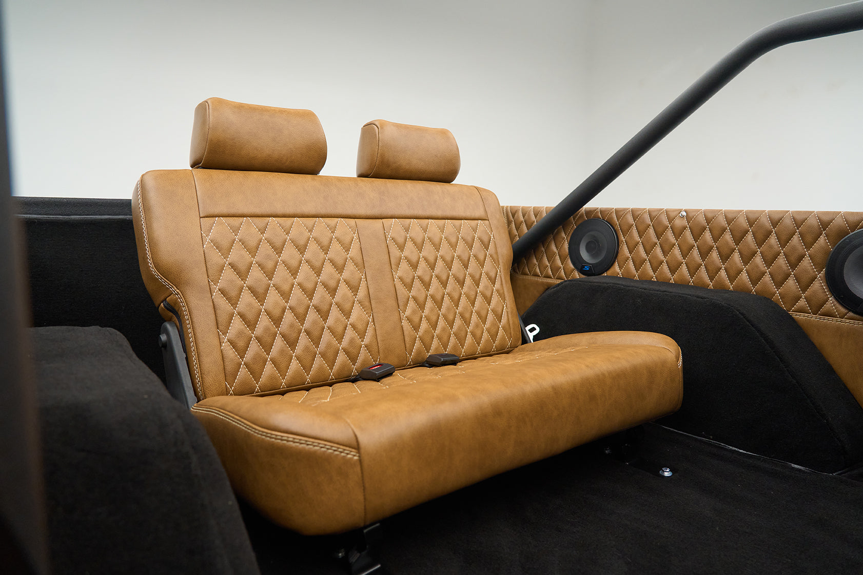 Rear tan leather quilted bench seat with black carpet and two round speakers