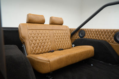 Rear tan leather quilted bench seat with black carpet and two round speakers