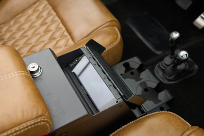Car center console with brown leather seats, cup holders, key lock, and an open compartment showing a screen inside.