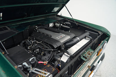 Classic Ford Bronco engine bay with a modern 5.0-liter Coyote V8 engine installed, showing green patina body.