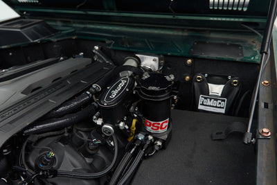 Engine compartment showing Wilwood and PSC power steering components with a FoMoCo parts bag in the background.