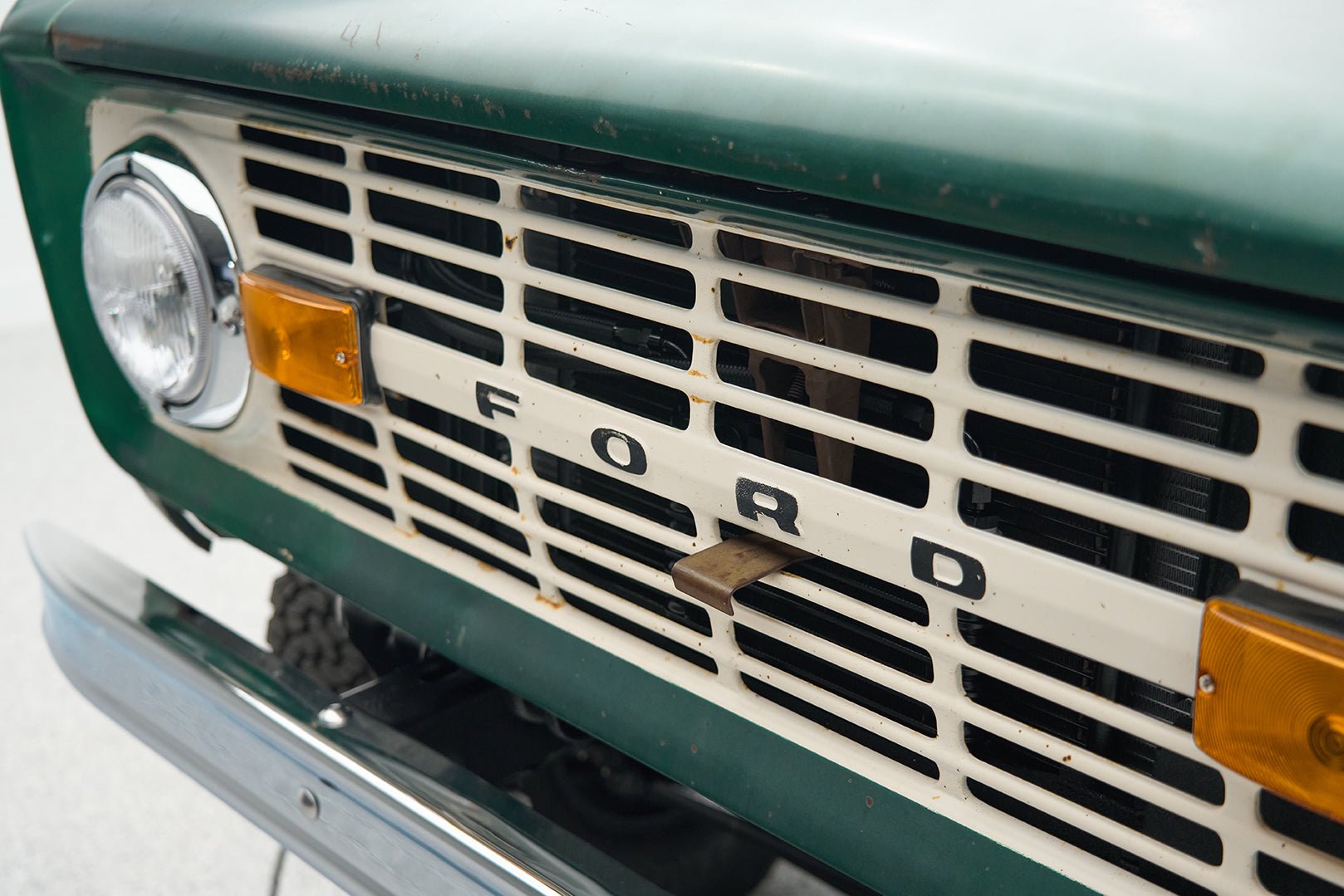 Close-up of the front grille and headlight of a green Classic Ford Bronco with a white "FORD" emblem.