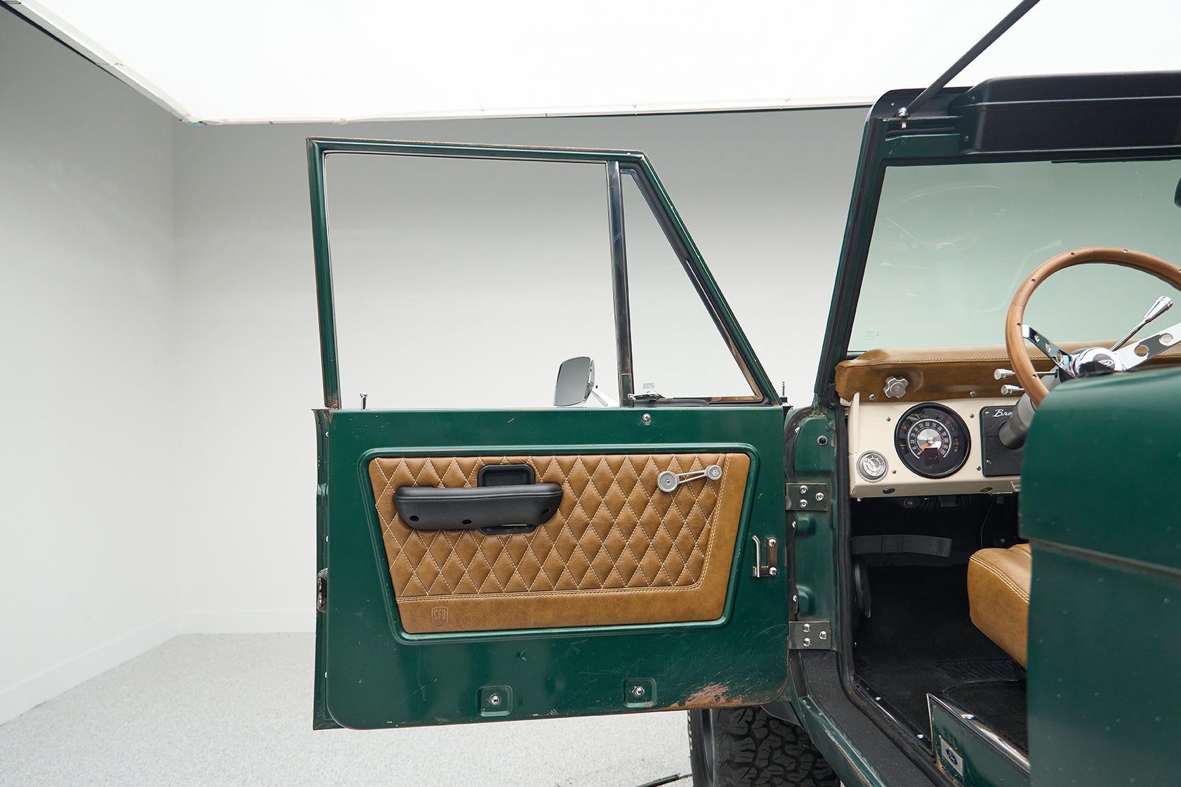 Open green door of Classic Ford Bronco showing diamond-stitched tan leather interior panel.