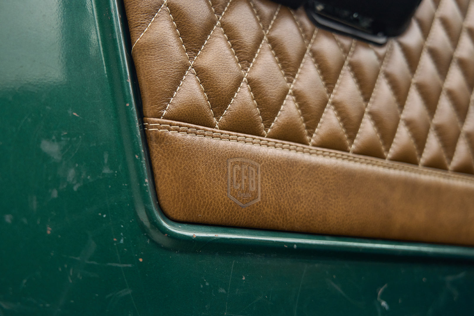 Close-up of diamond-stitched tan leather interior door panel with embossed CFB logo on Classic Ford Bronco.