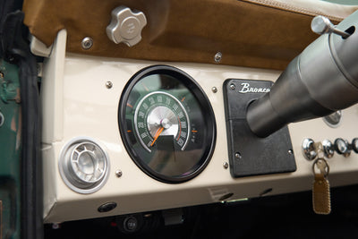 Tan dashboard and steering wheel with Classic Ford Bronco badge and manual gear shifter inside vehicle.