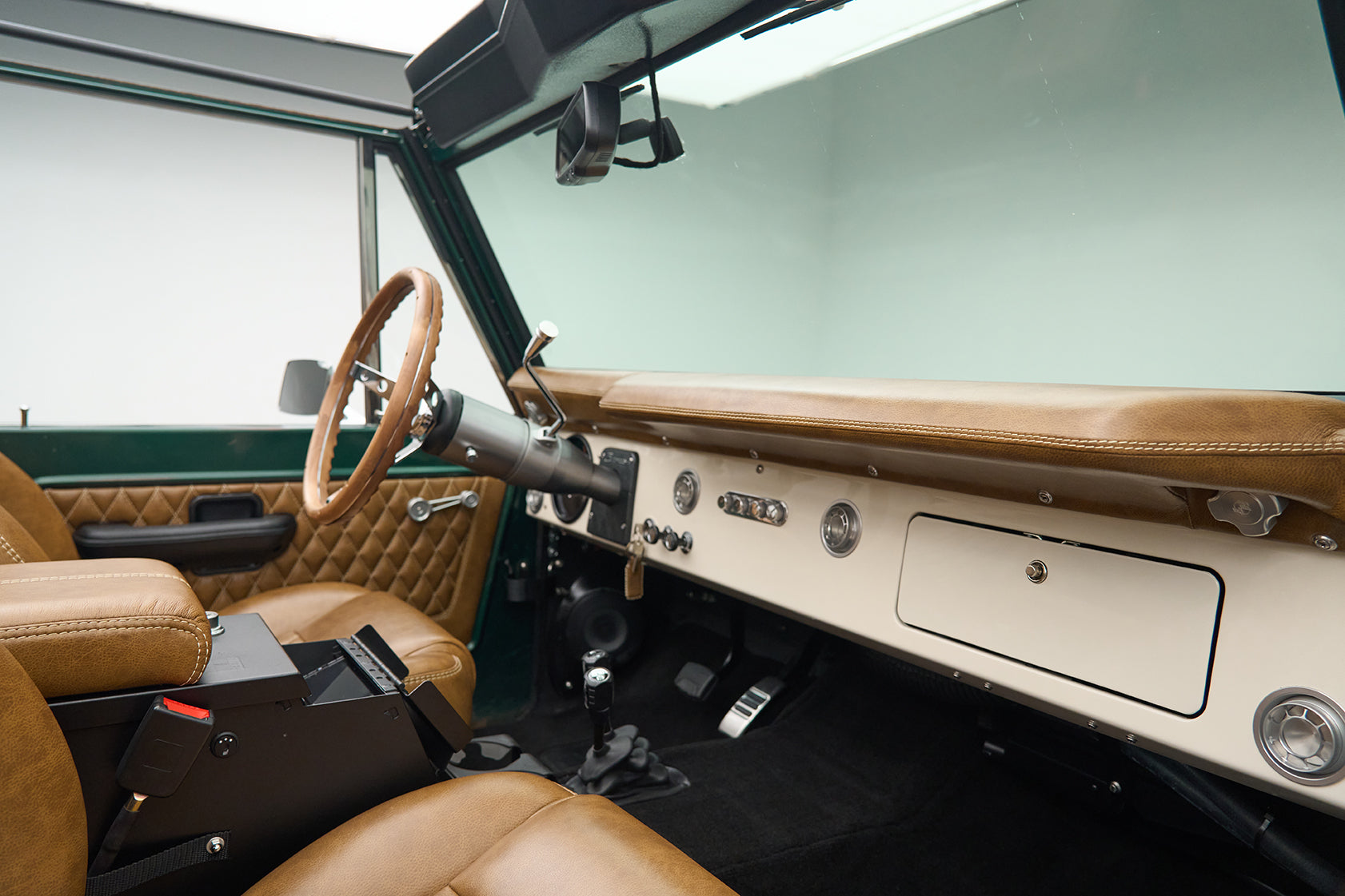 Interior view of Classic Ford Bronco cabin showing tan dashboard, steering wheel, and front seats.
