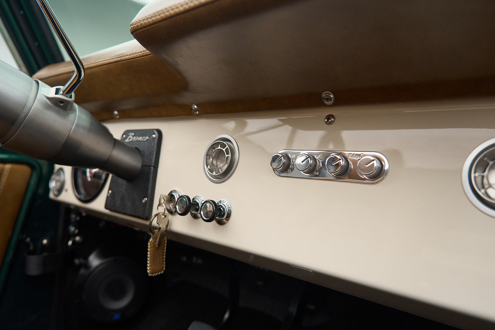 Control knobs and vents on cream dashboard with hanging key and leather key fob in Classic Ford Bronco.