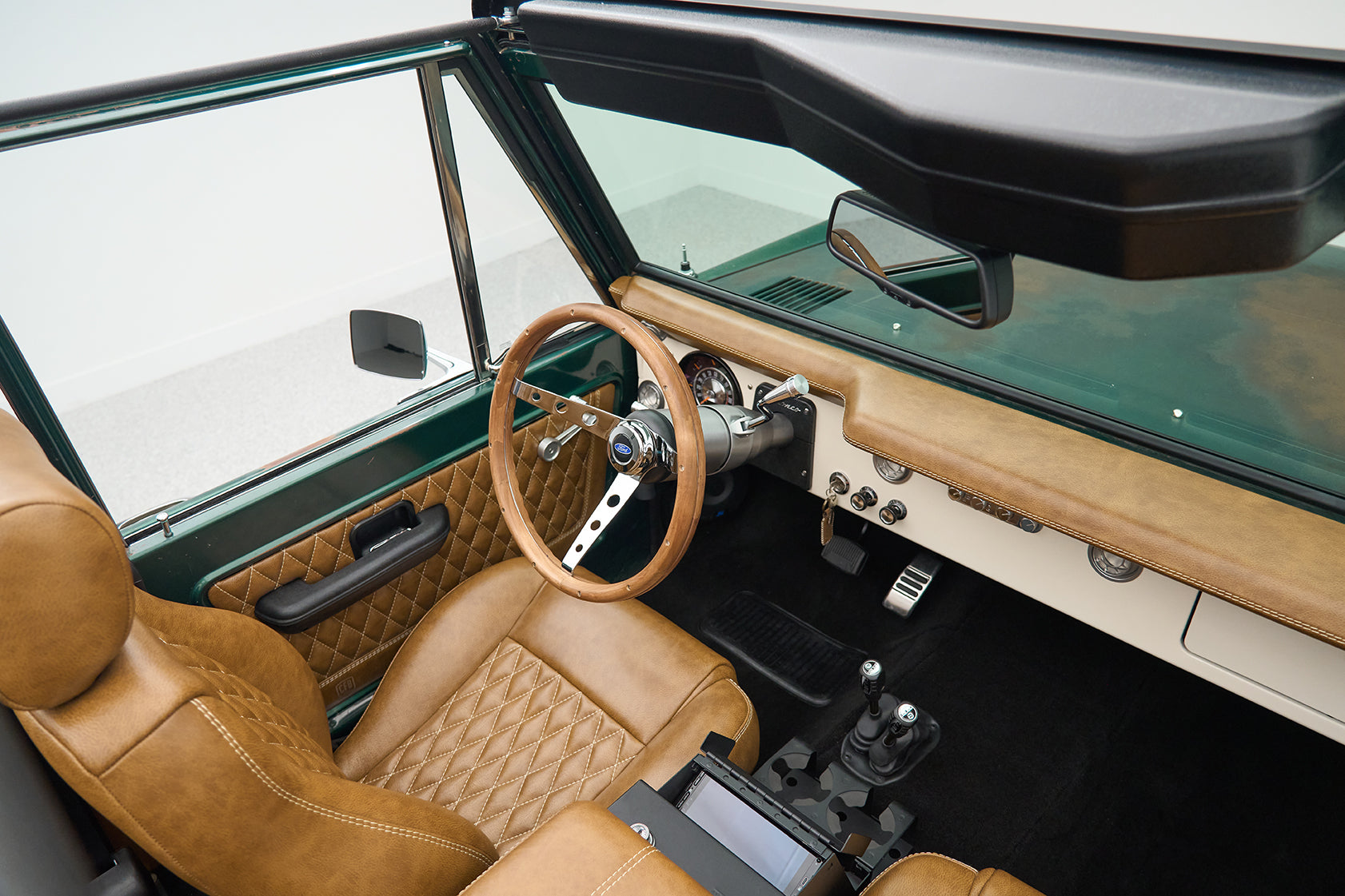 Interior of Classic Ford Bronco showing tan quilted leather front seats, steering wheel, and dashboard.