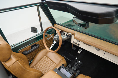 Interior of Classic Ford Bronco showing tan quilted leather front seats, steering wheel, and dashboard.