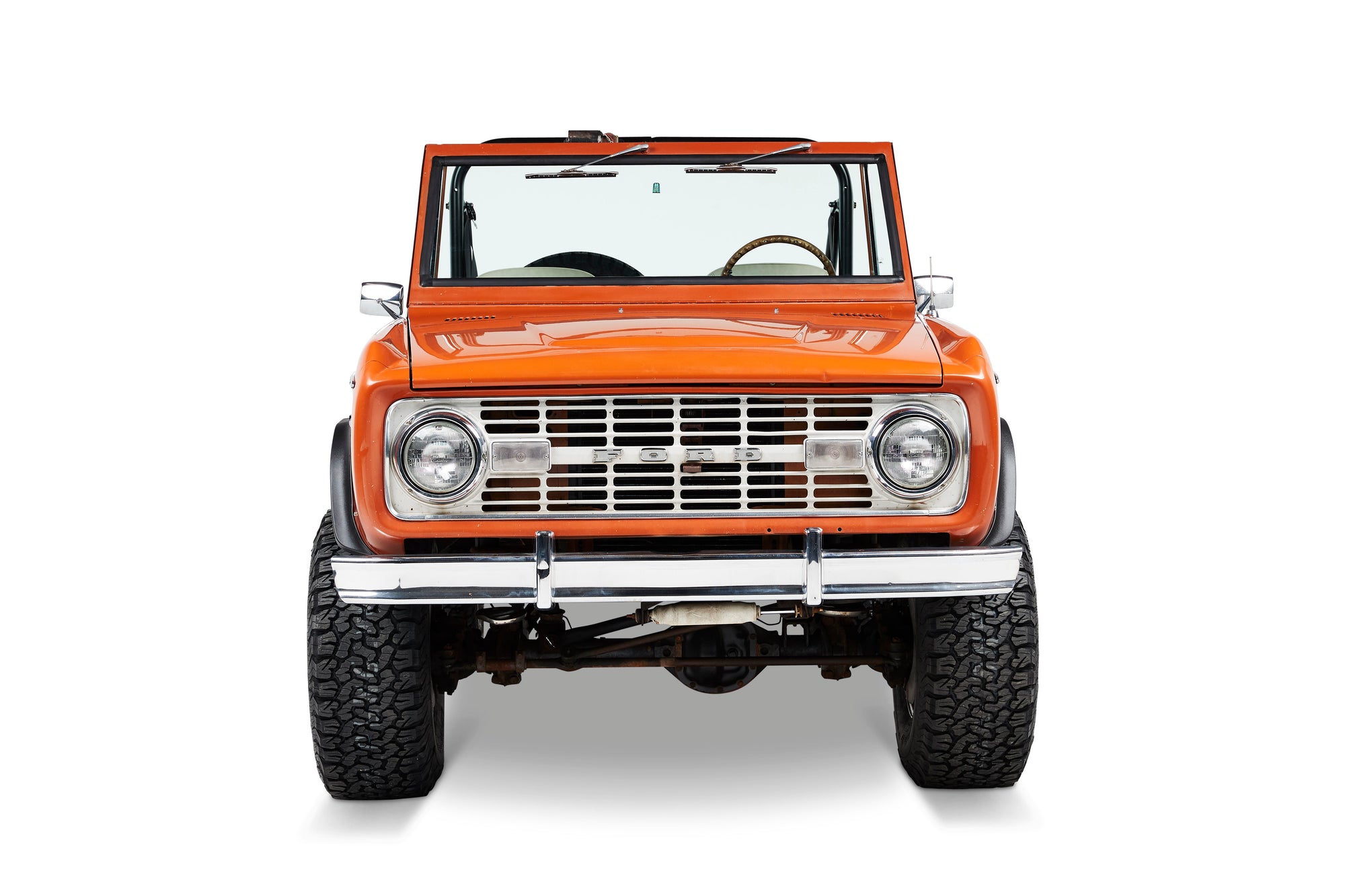 Front view of orange Classic Ford Bronco showing grille, headlights, and windshield.