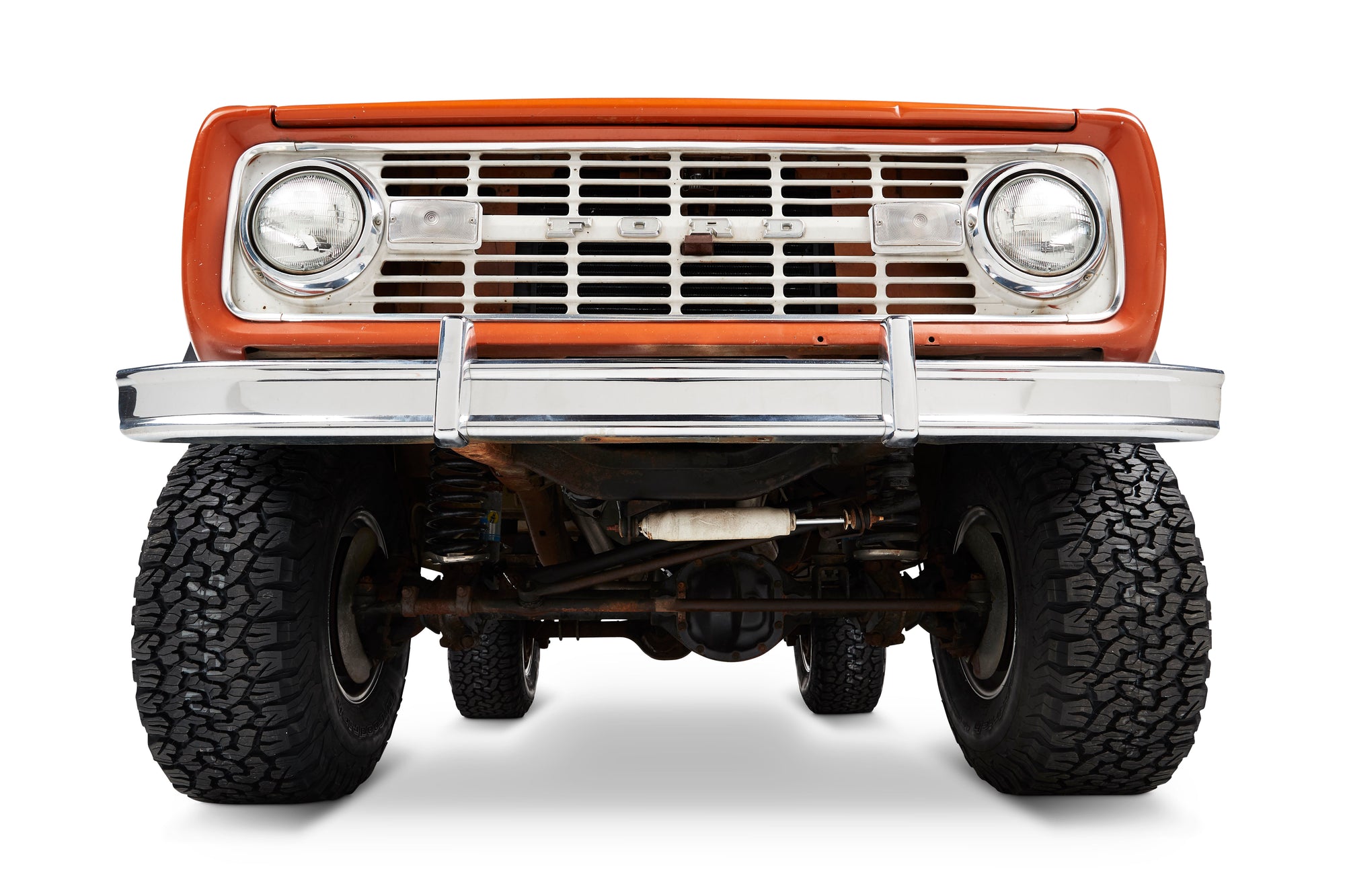 Front view of orange Classic Ford Bronco showing bumper, grille, and headlights.