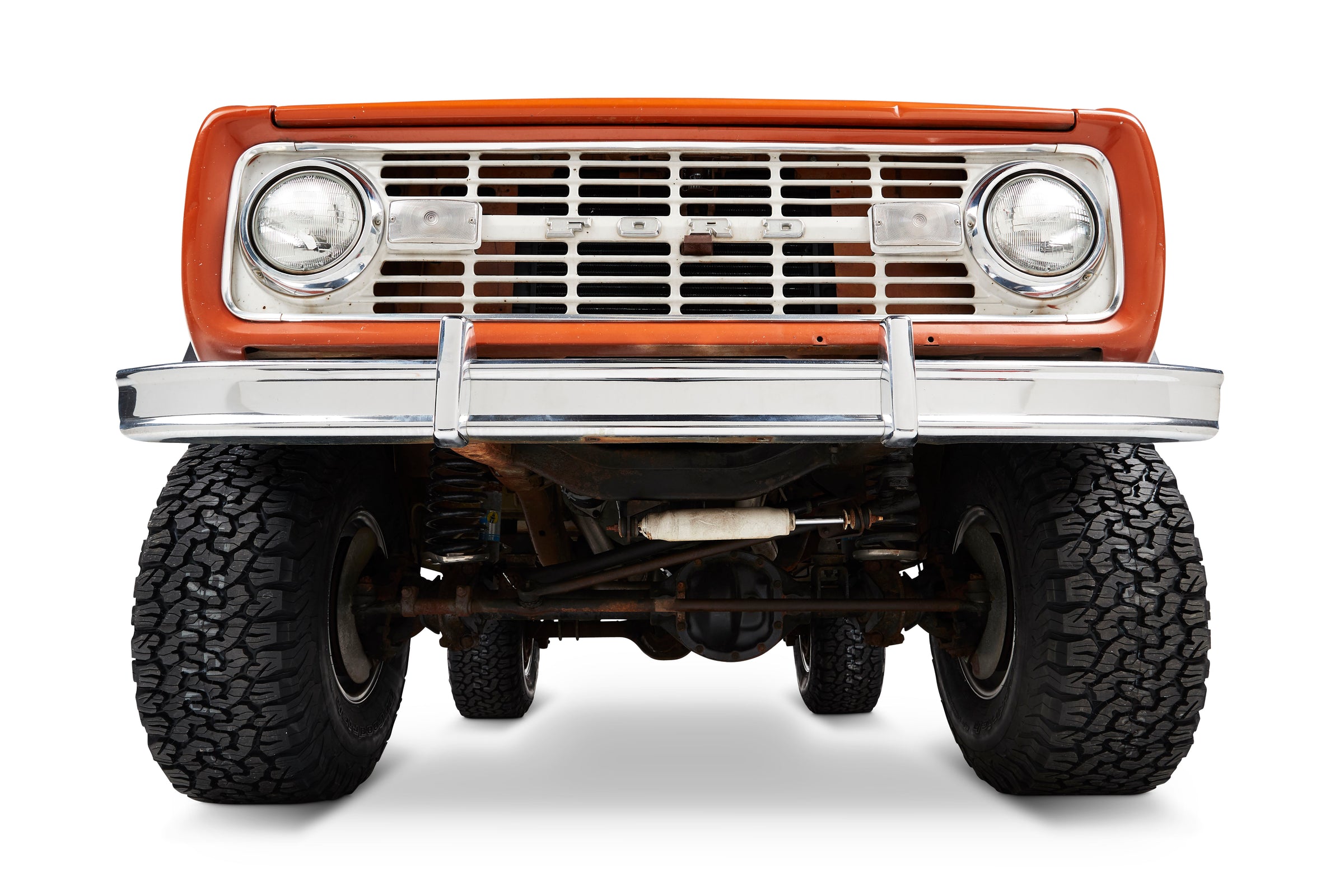 Front view of orange Classic Ford Bronco showing bumper, grille, and headlights.