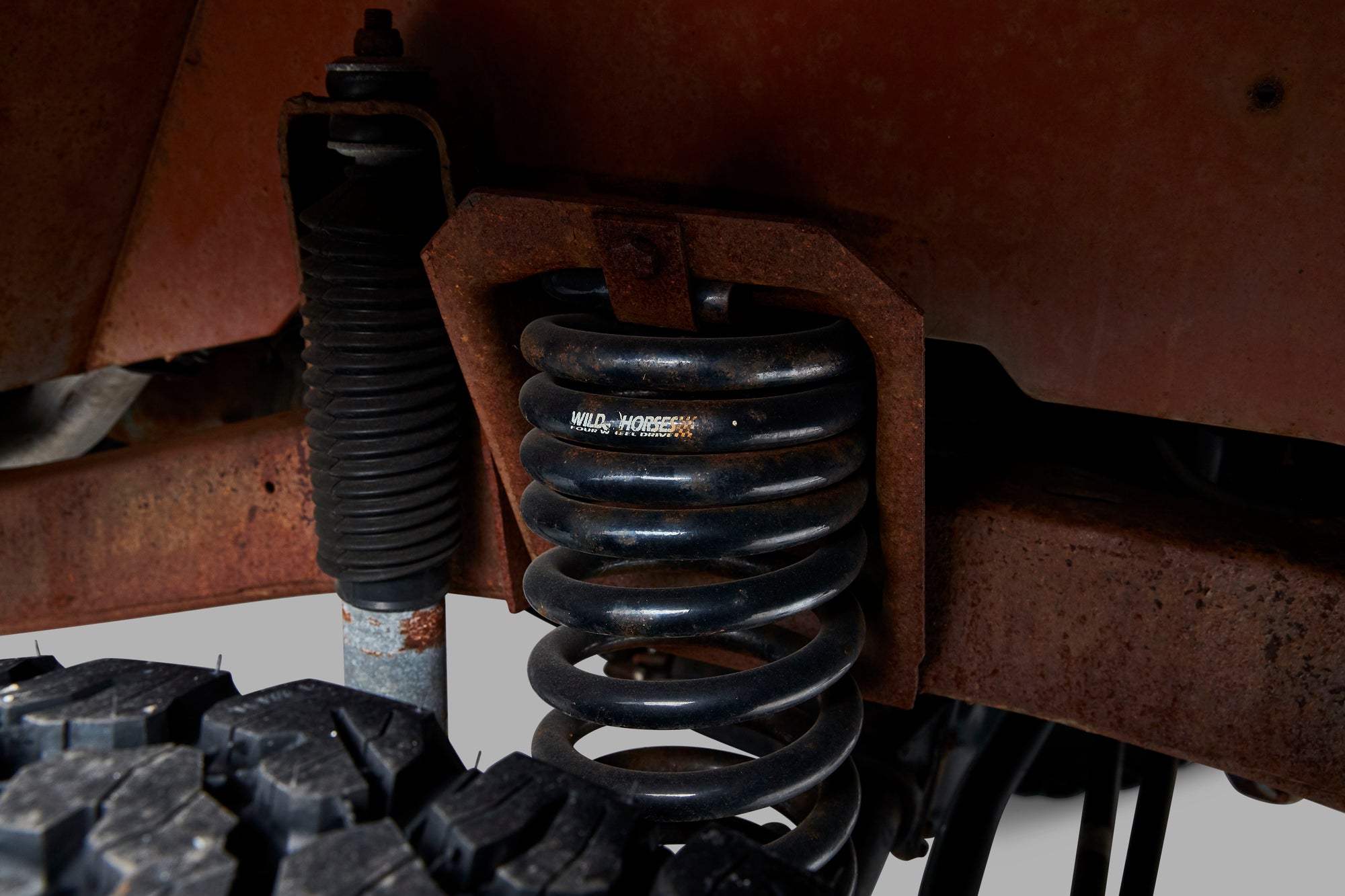 Close-up of black coil spring and shock absorber on vehicle suspension above tire.